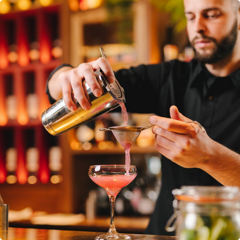 A bartender pouring a cocktail through a strainer into a margarita glass