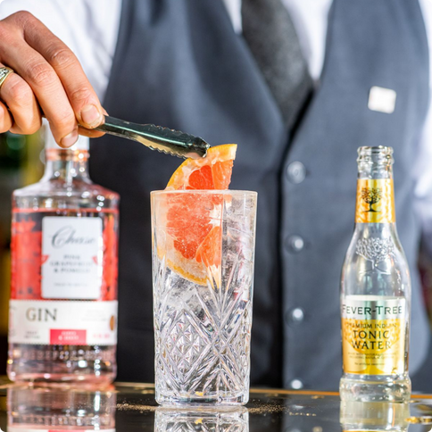 A bartender adding a grapefruit slice to a G&T
